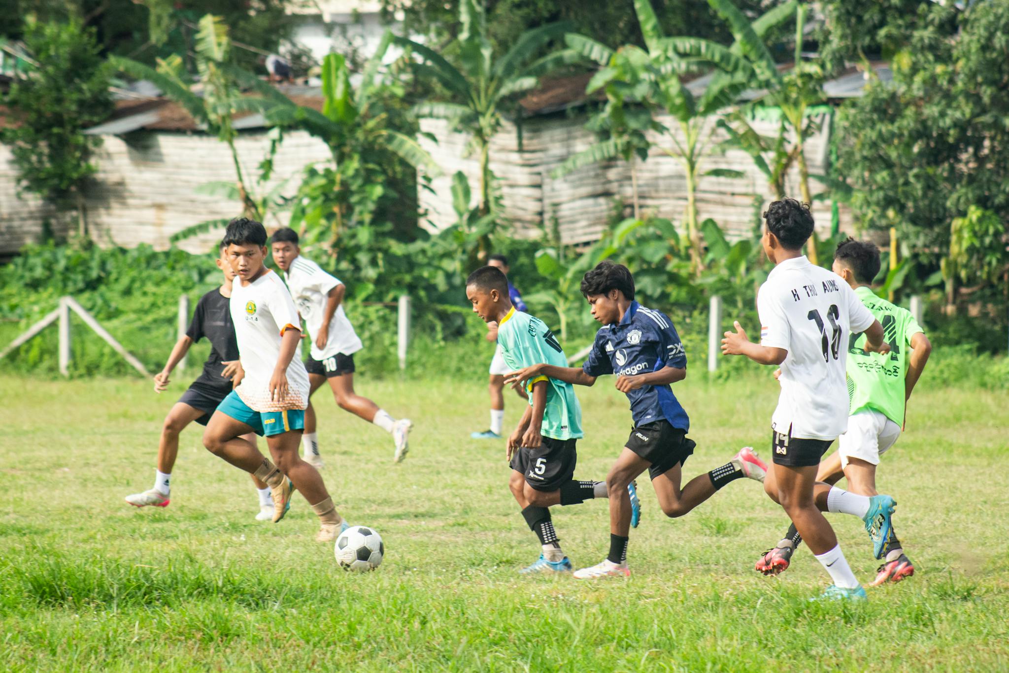Young boys playing an intense soccer match on a grassy field in Myawaddy, Myanmar.